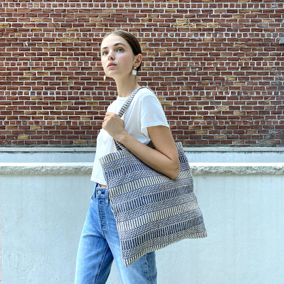 Woman holding a patterned tote bag against a brick wall.