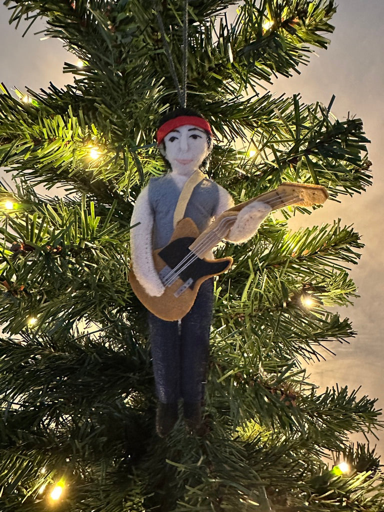 Ornament of a person playing guitar hanging on a Christmas tree.