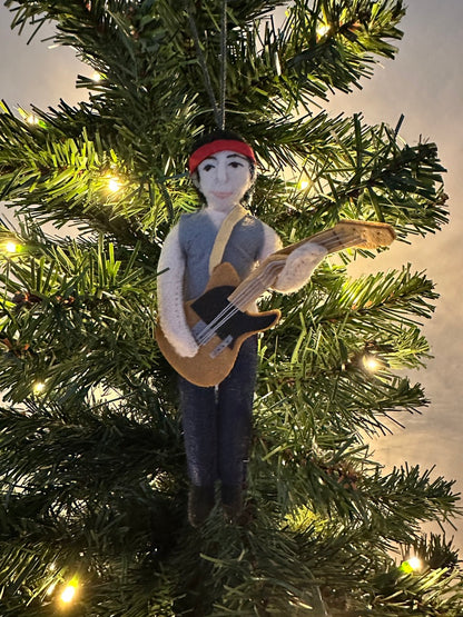Ornament of a person playing guitar hanging on a Christmas tree.