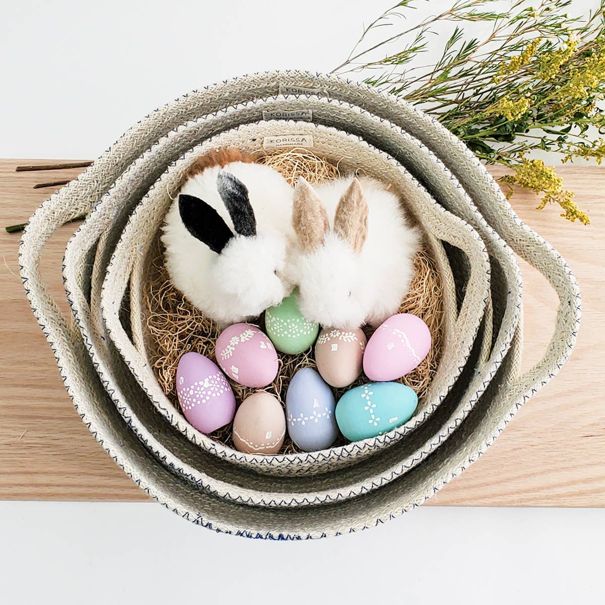 Bunny plush toy with pastel Easter eggs in a woven basket on a wooden surface.