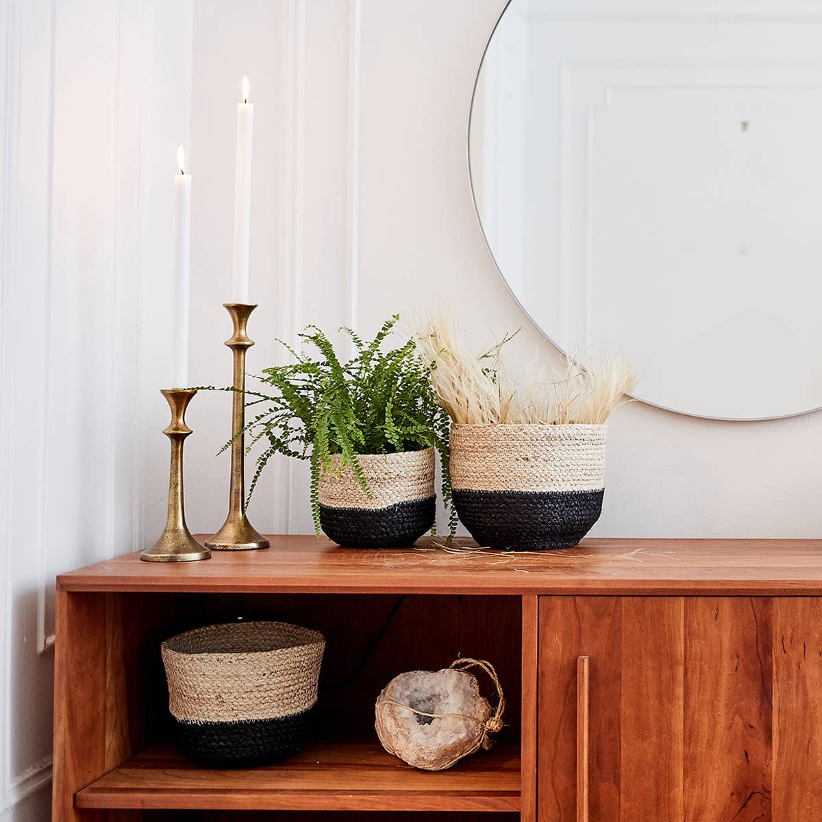 Decorative setup with woven baskets, candles, and a plant on a wooden surface.