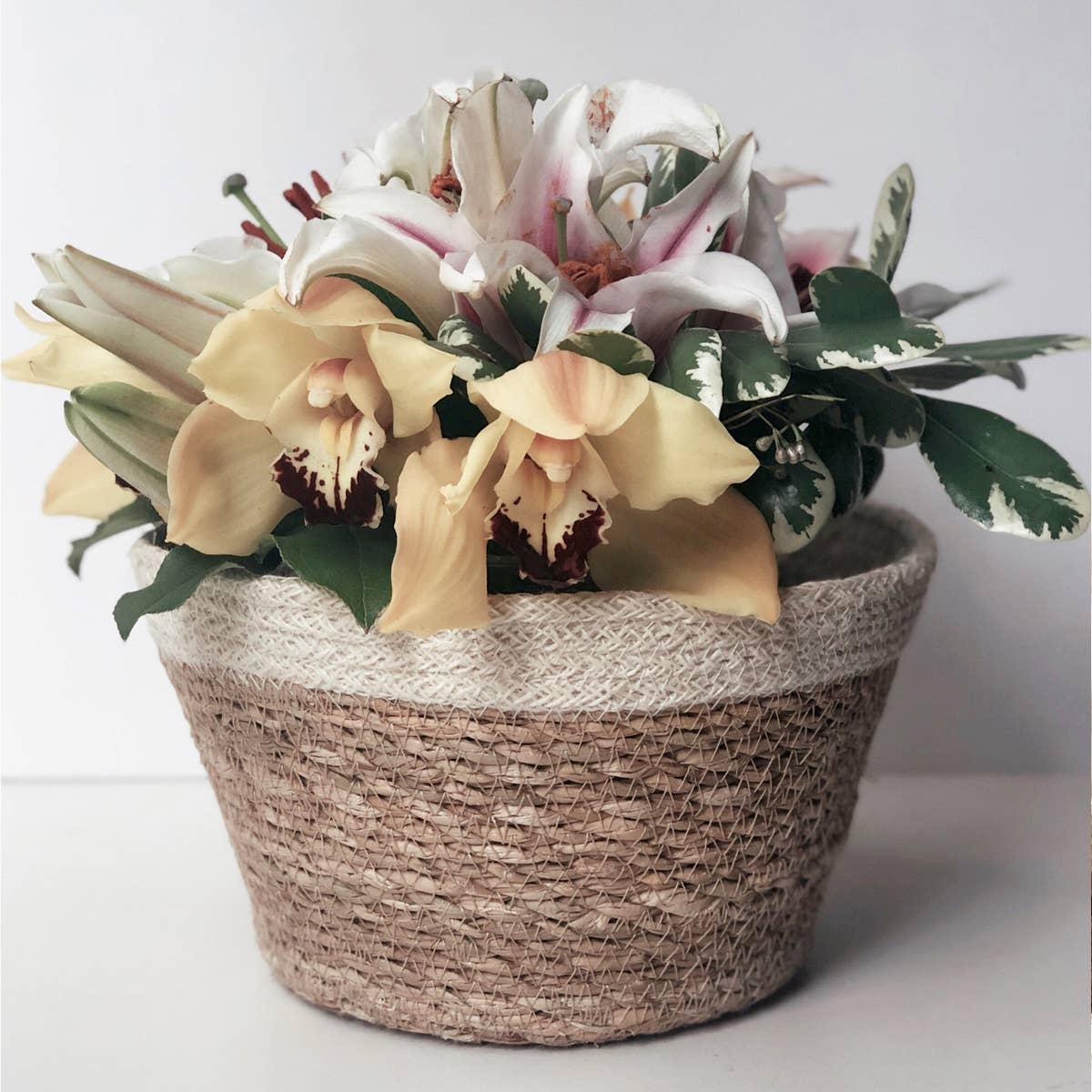 Floral arrangement in a textured woven pot on a light background