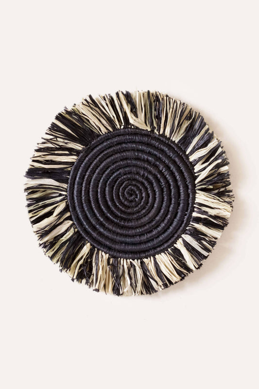 Round woven coaster with black spiral center and beige frayed edges on a white background