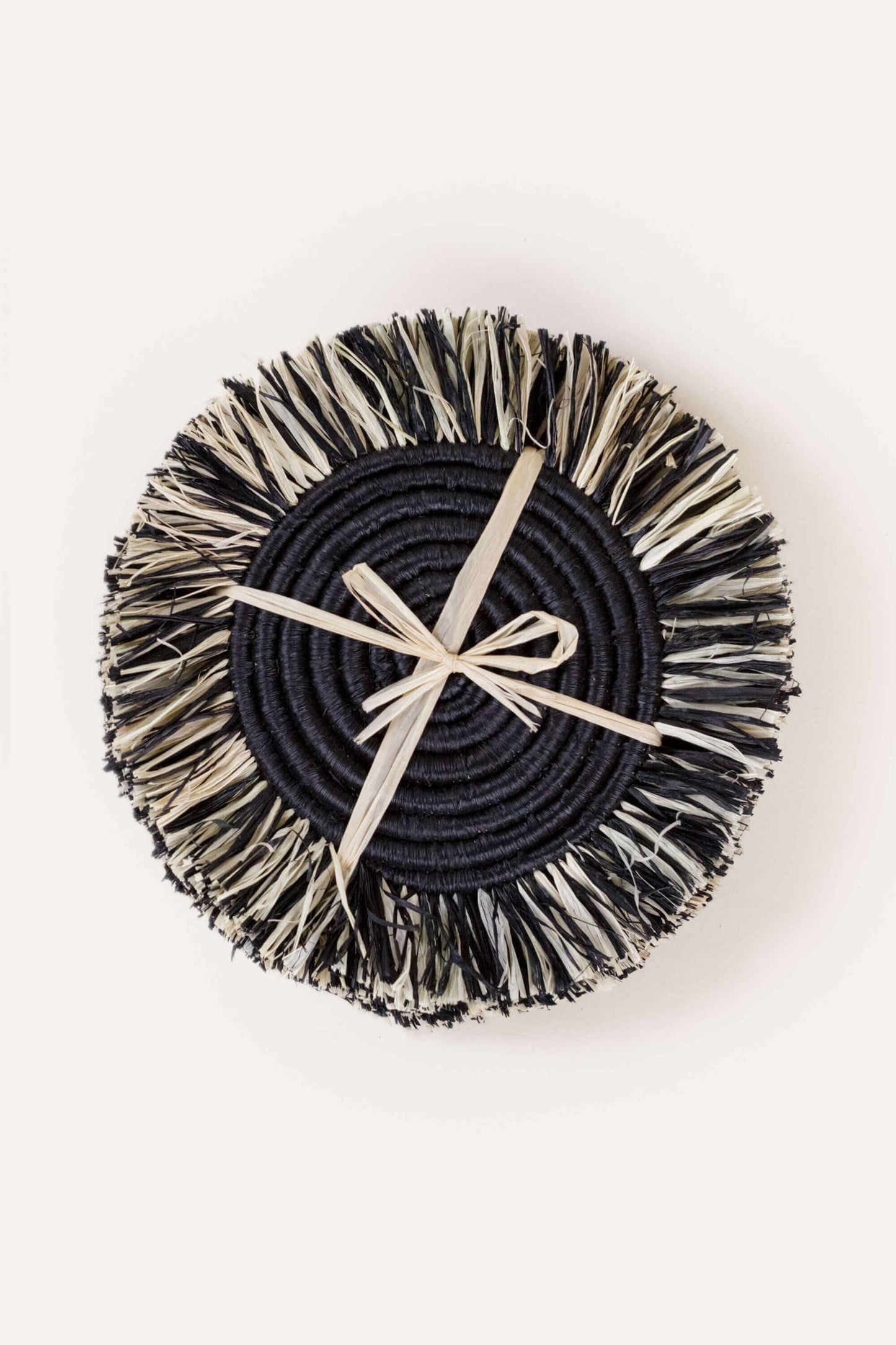 Round woven coaster with black center and beige rim on a white background