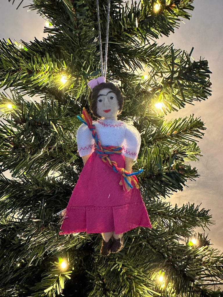 Ornament of a person in a pink dress hanging on a Christmas tree.