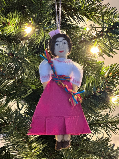 Decorative ornament of a woman in a pink dress hanging on a Christmas tree.