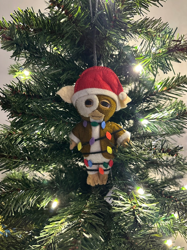 Brown felt ornament with a Santa hat wrapped in rainbow lights hanging on a Christmas tree.
