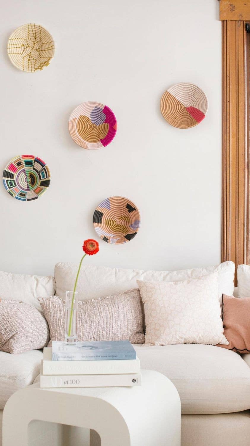 Decorative wall plates on a white wall above a sofa with a small table and books.