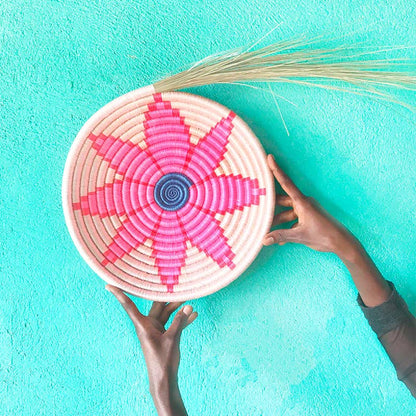 Woven basket with pink and blue pattern held by hands against a turquoise background