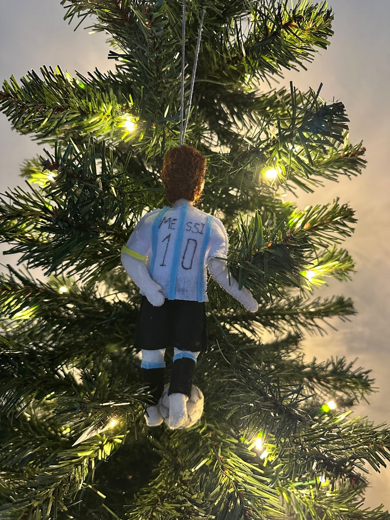 Christmas tree ornament of a soccer player in a blue jersey with the number 10, hanging on a lit Christmas tree.