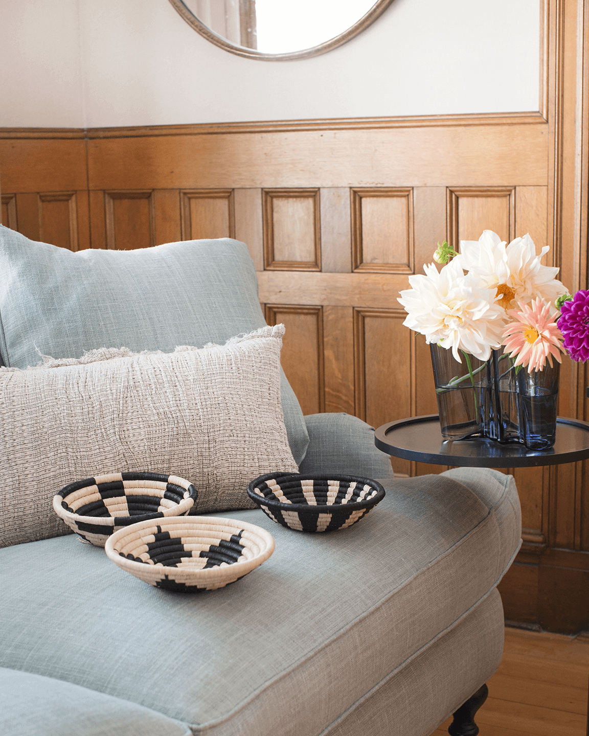 Decorative bowls on a sofa with a vase of flowers on a side table in a room with wooden paneling.
