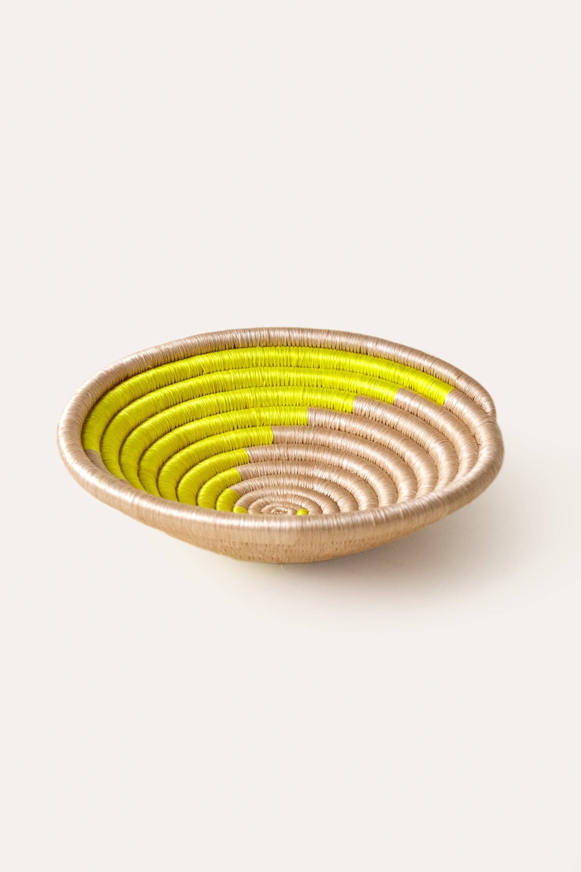Woven bowl with concentric circle pattern in green and brown on a white background