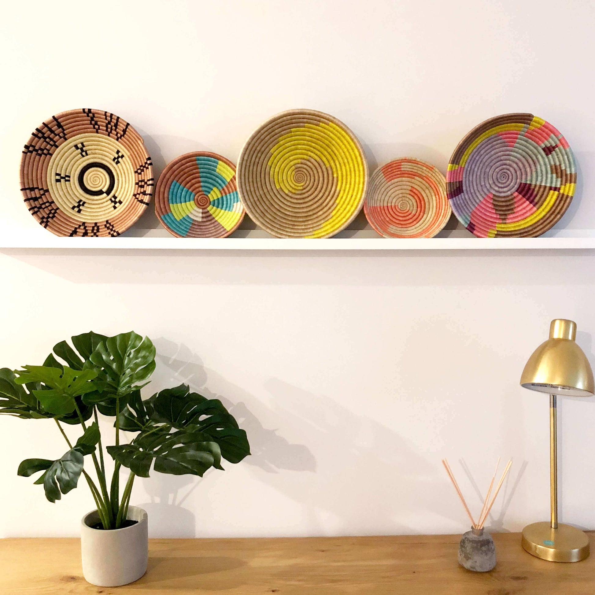 Colorful woven baskets on a shelf with a plant and lamp in the foreground.