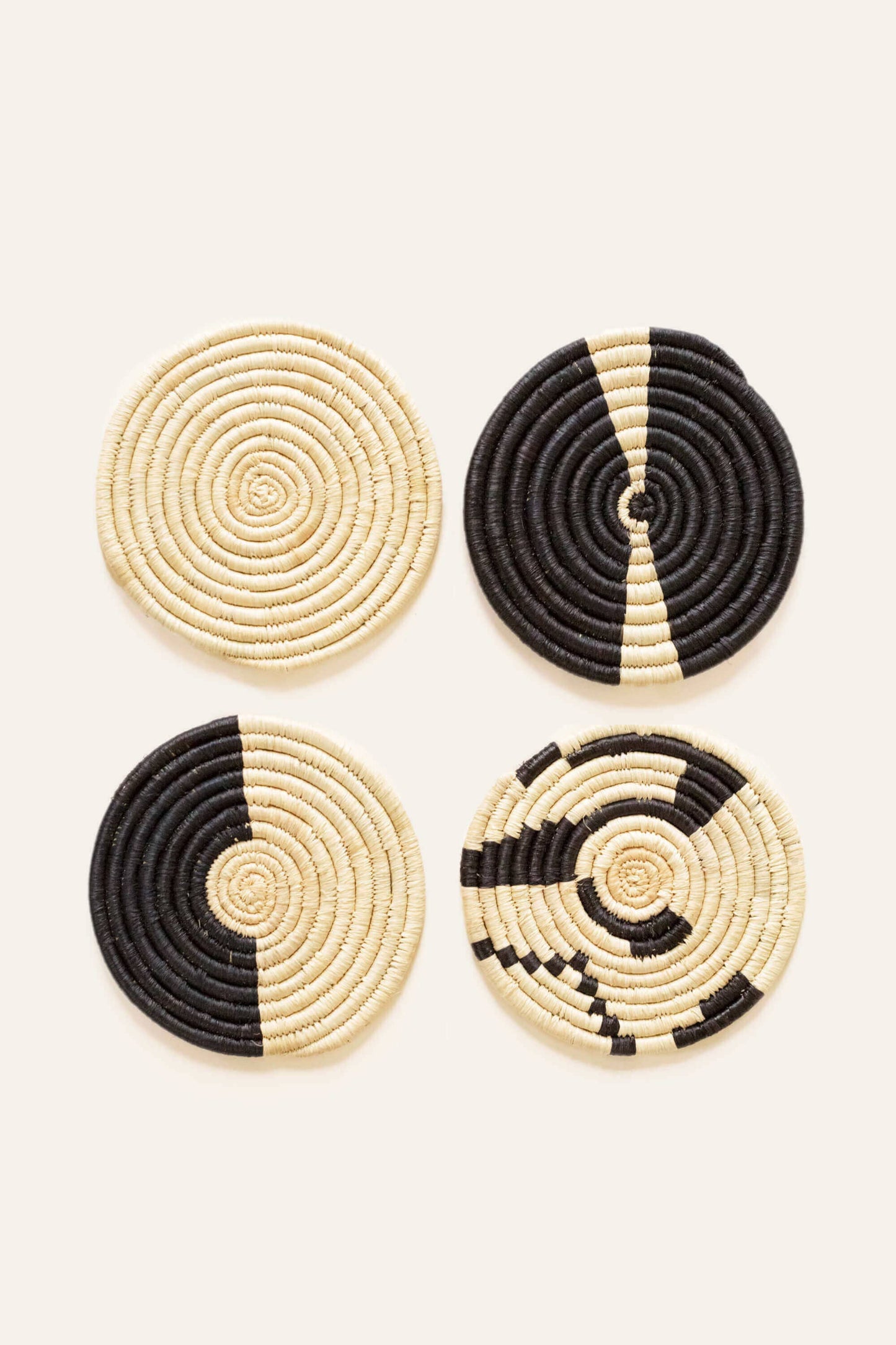Four woven coasters with black and beige patterns on a white background