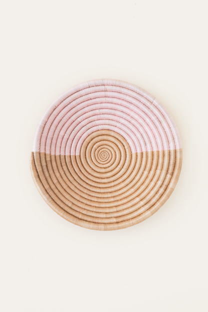 Round woven coaster with pink top and beige bottom on a white background