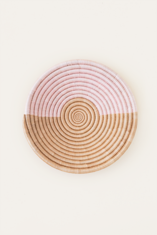 Round woven coaster with pink top and beige bottom on a white background