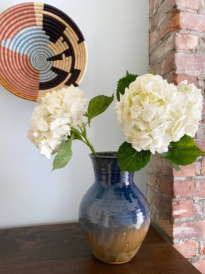 Blue vase with white flowers against a brick wall and decorative basket.