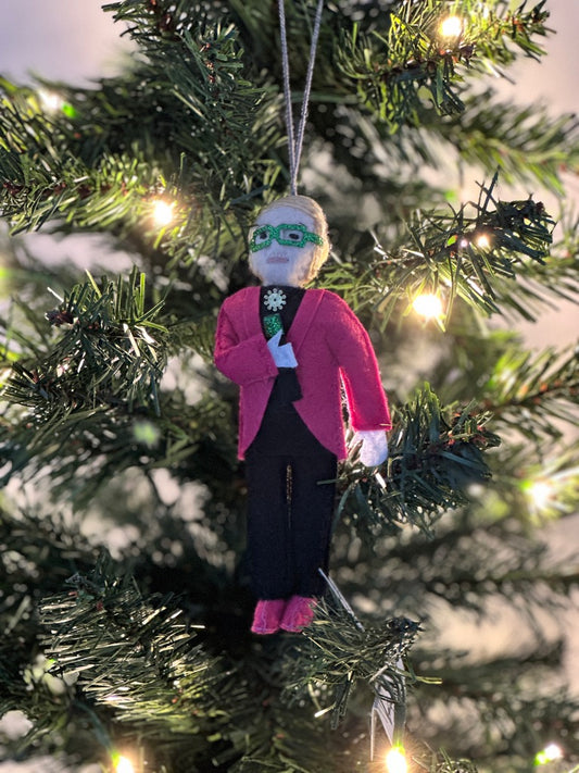 Decorative ornament of a person in a pink jacket hanging on a Christmas tree.