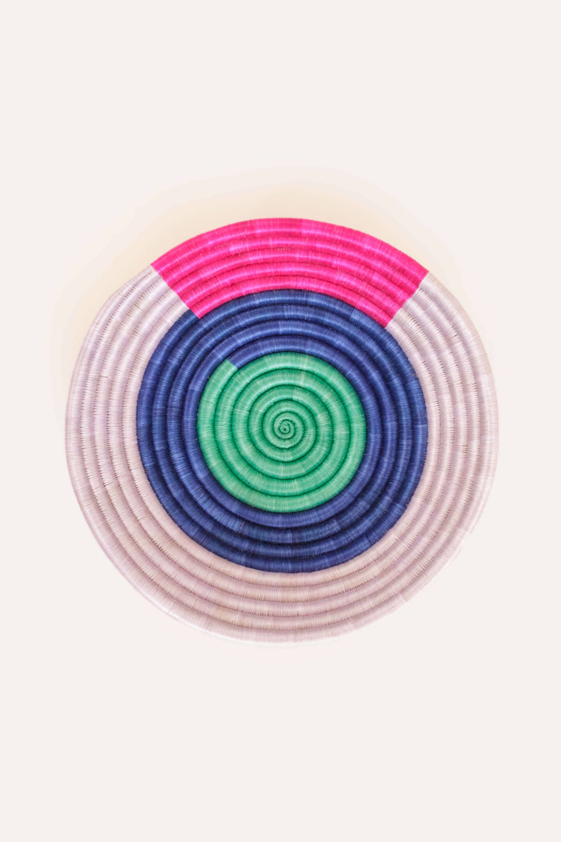 Round woven coaster with concentric circle pattern in pink, blue, and green on a white background