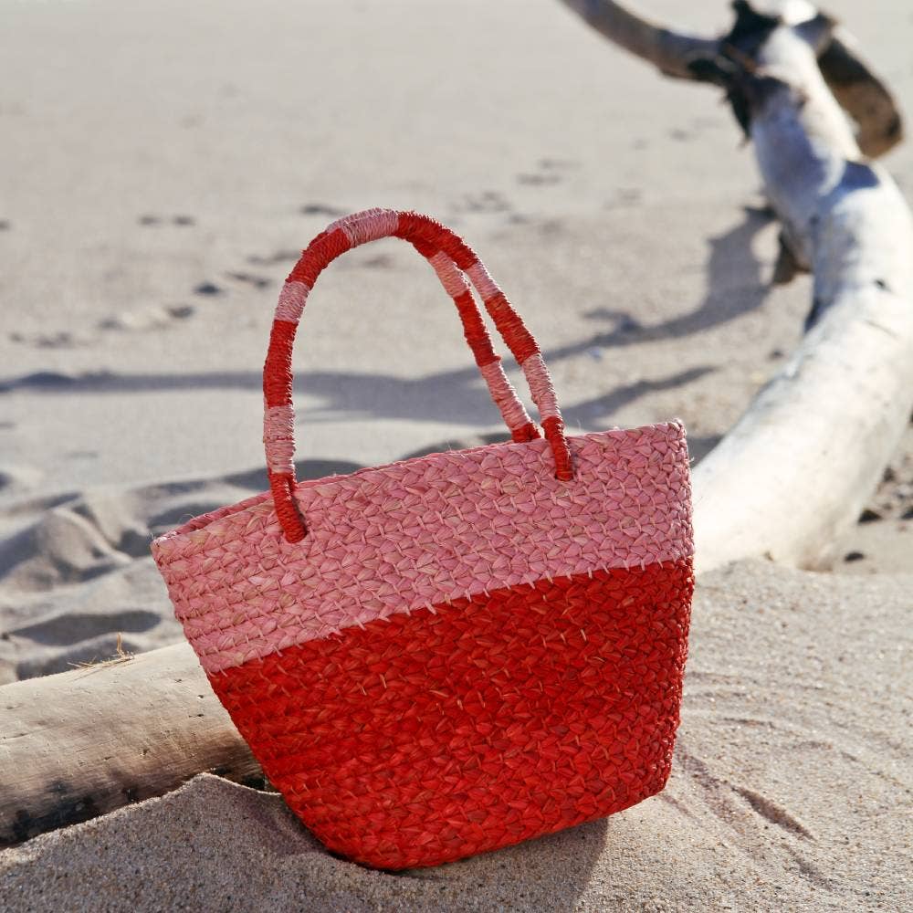 Red woven bag on a sandy beach with driftwood.