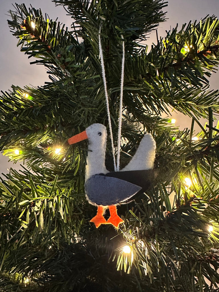 Seagull ornament hanging on a decorated Christmas tree with lights.