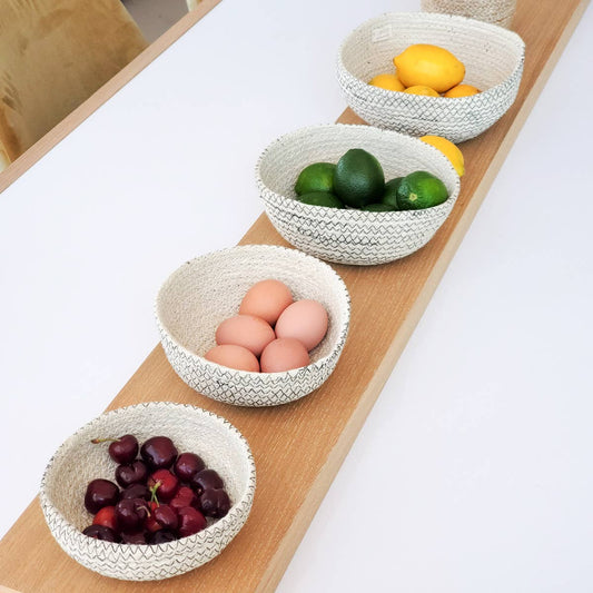 Set of woven bowls containing fruits and eggs on a wooden surface.