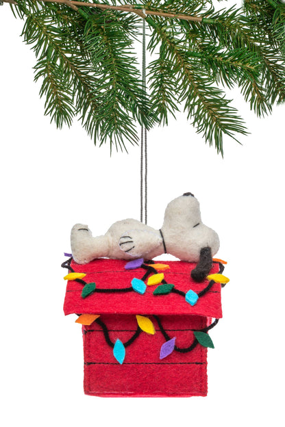 Christmas ornament with Snoopy and Woodstock on a red doghouse with lights, hanging from a tree branch.