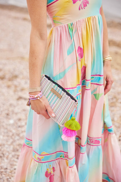 Woman in a colorful dress holding a beaded clutch with tassels on a beach.