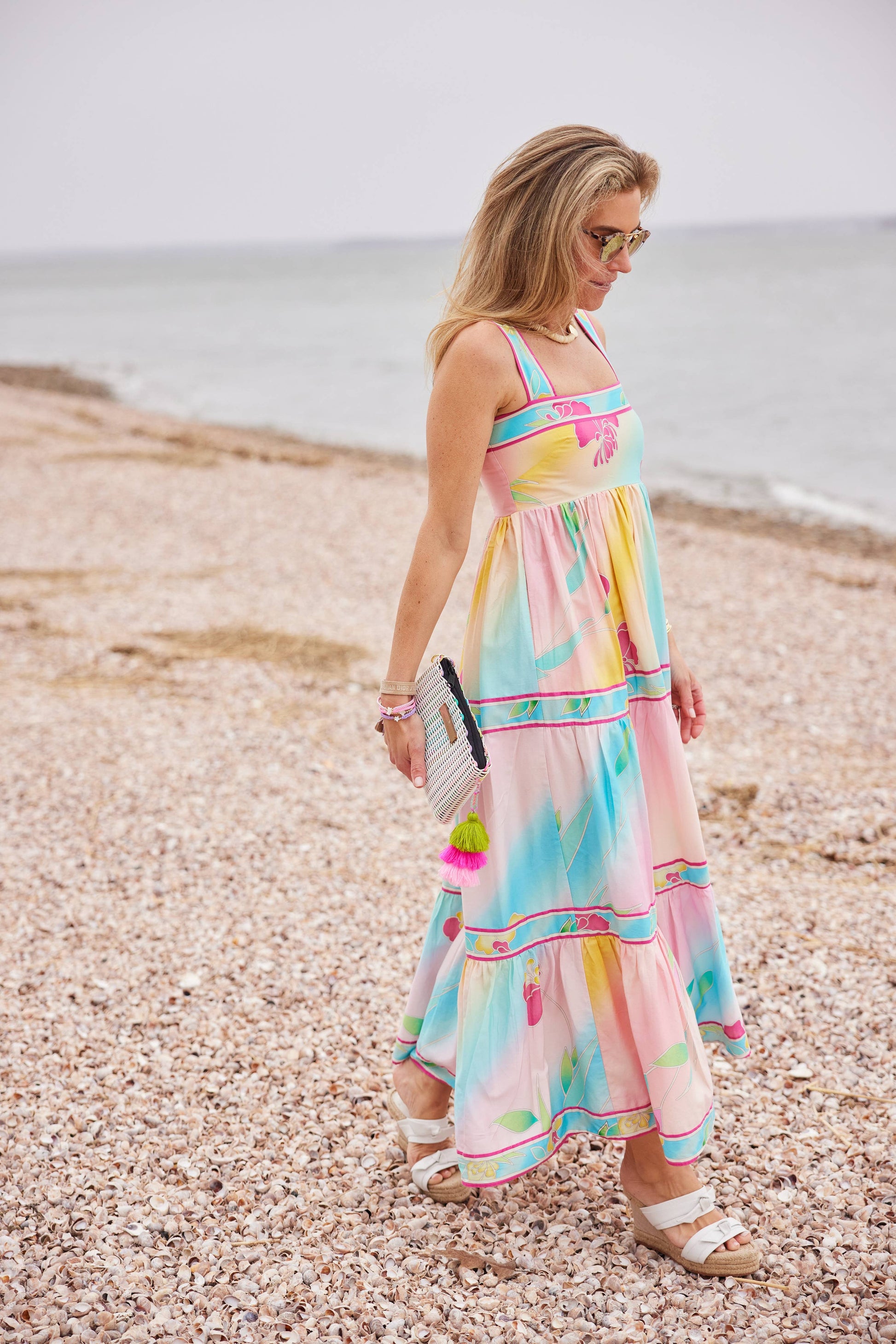 Woman in a colorful dress standing on a pebbly beach.