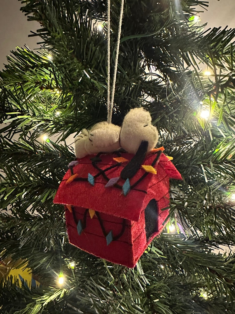 Decorative Christmas ornament with a red house and small figure on a lit Christmas tree.