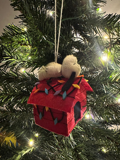 Decorative Christmas ornament with a red house and small figure on a lit Christmas tree.