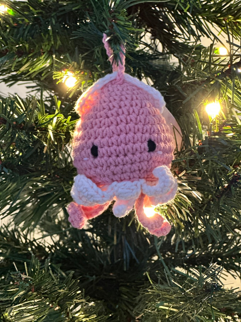 Pink crochet squid ornament hanging on a Christmas tree.