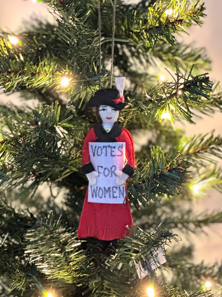 Suffragate ornament wearing a red and black coat and holding a "Votes for Women" sign hanging on a Christmas tree.