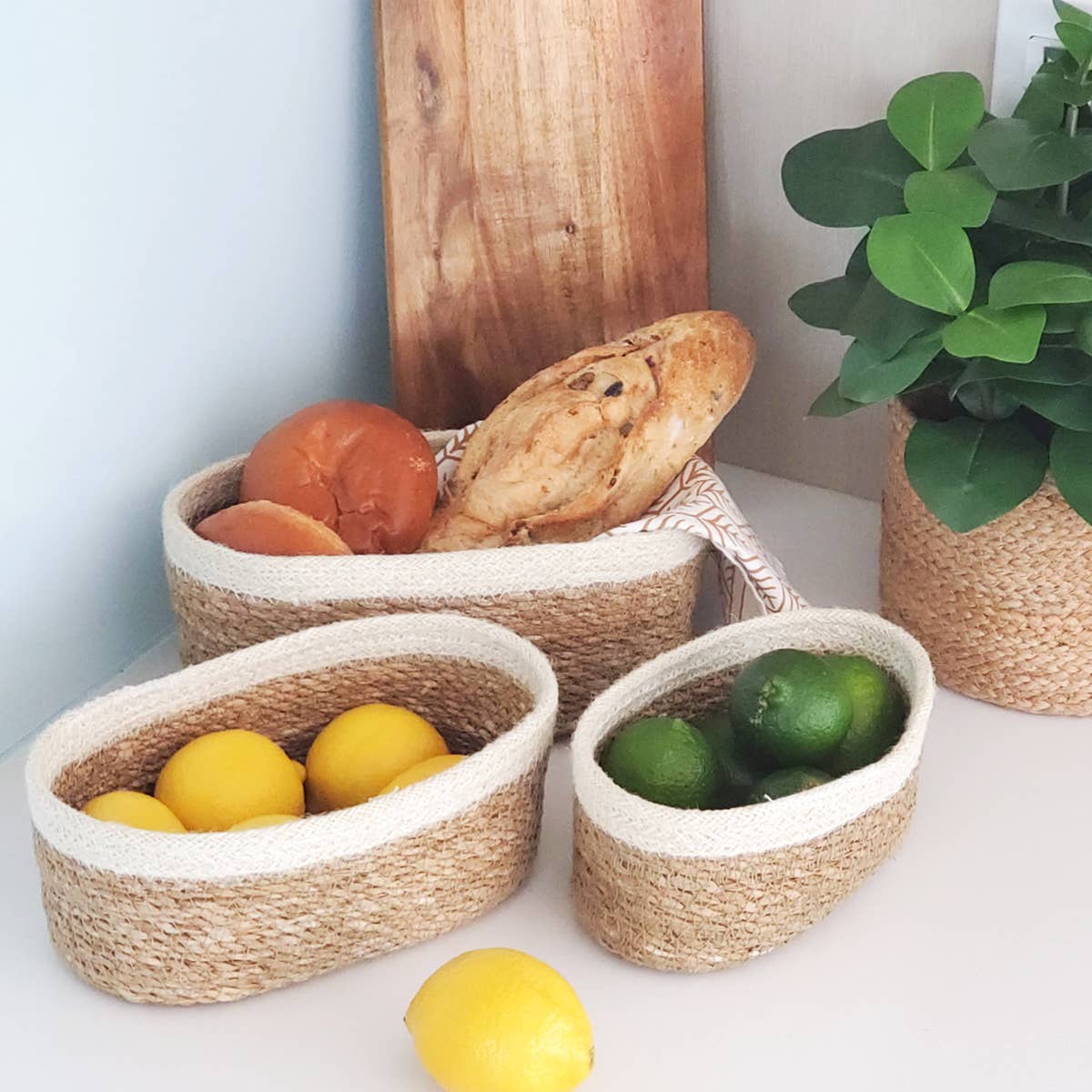 Three woven baskets with fruits and a plant on a light surface.