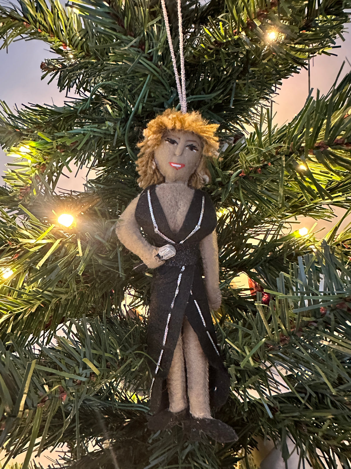 Decorative ornament hanging on a Christmas tree. Ornament is a female singer in a black dress holding a microphone.