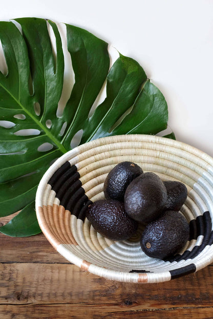 Avocados in a woven basket with a large leaf on a wooden surface