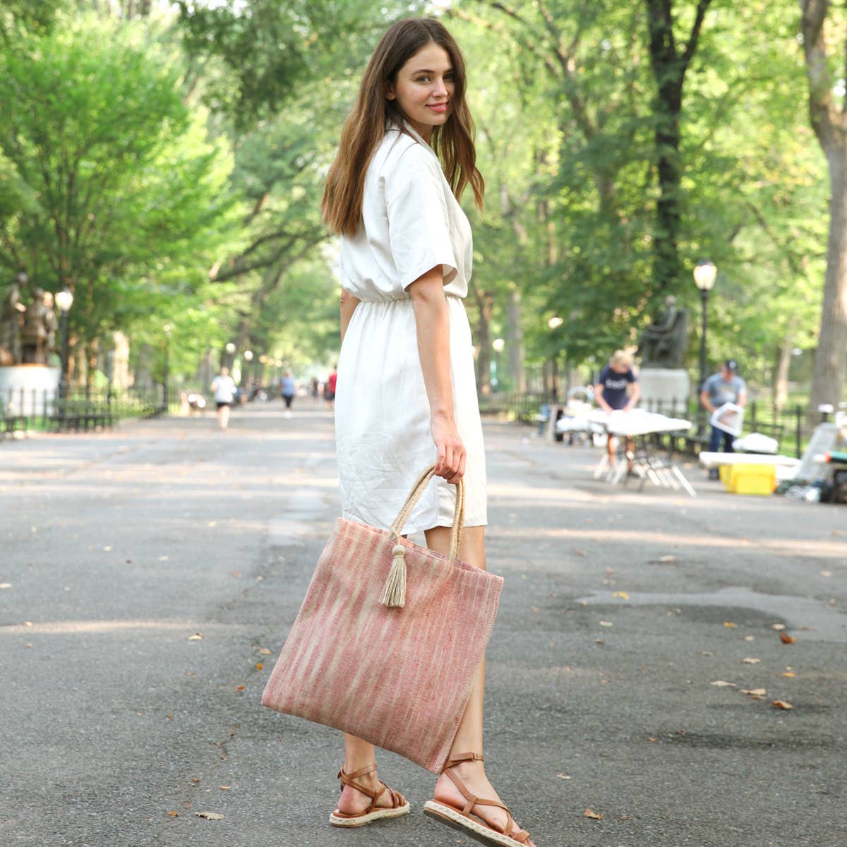 Woman in a white dress holding a pink tote bag in a park setting
