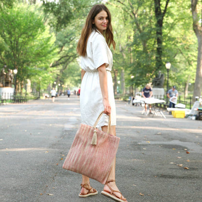 Woman in a white dress holding a pink tote bag in a park setting