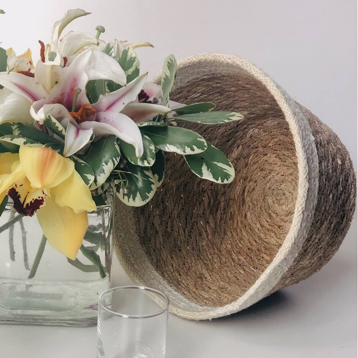 Woven basket with flowers and a glass on a light surface
