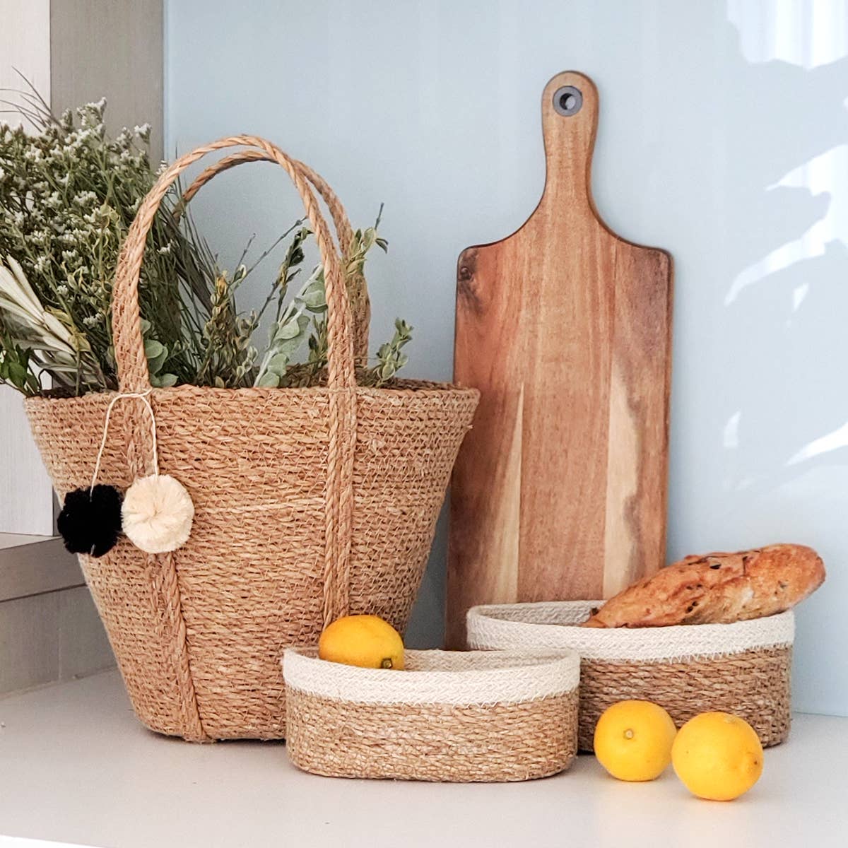 Woven baskets with a wooden cutting board and lemons on a light surface.