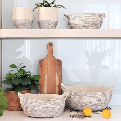Woven baskets, a wooden cutting board, and potted plants on a shelf against a white wall.