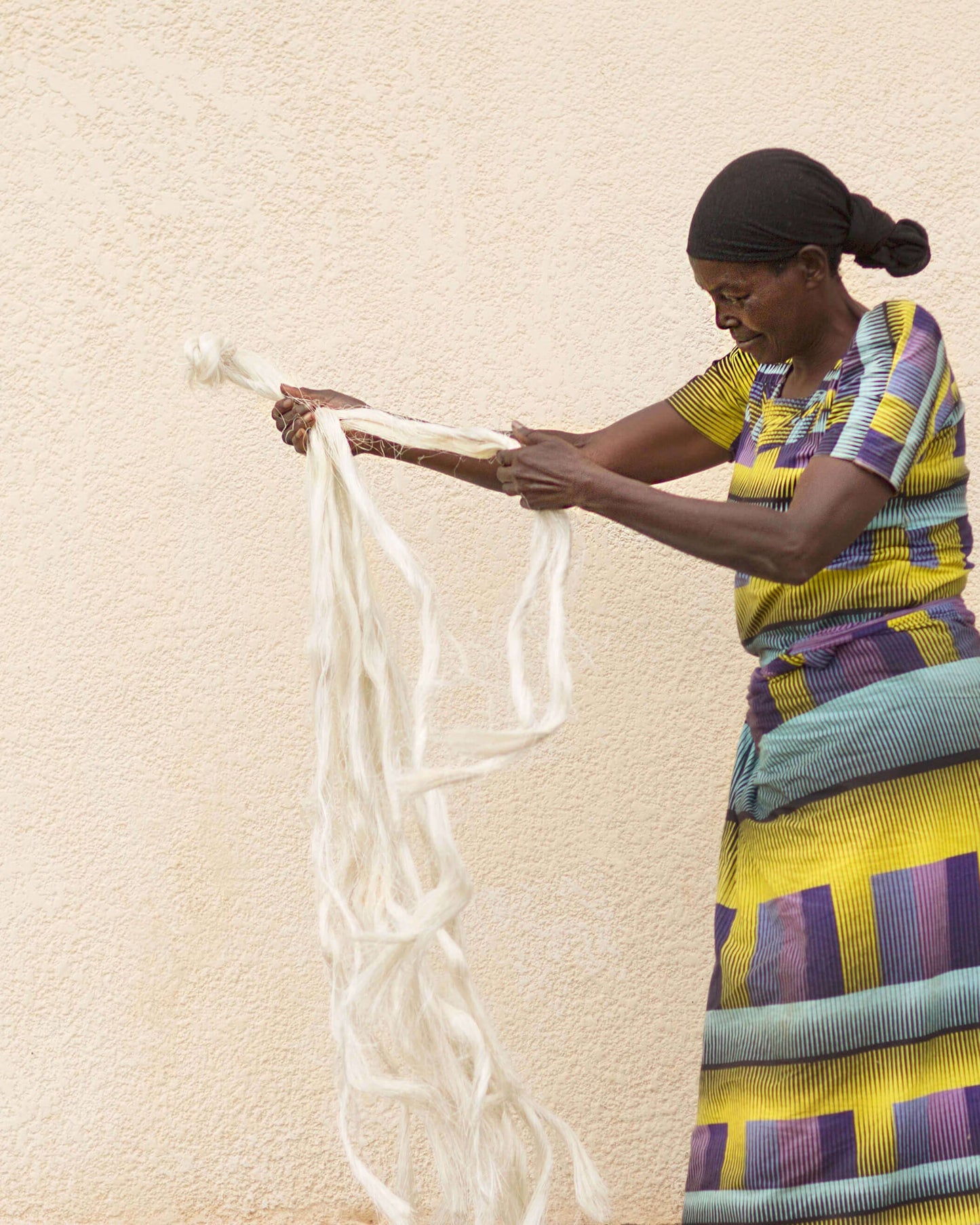 Woman in colorful traditional attire holding a white fabric against a beige wall