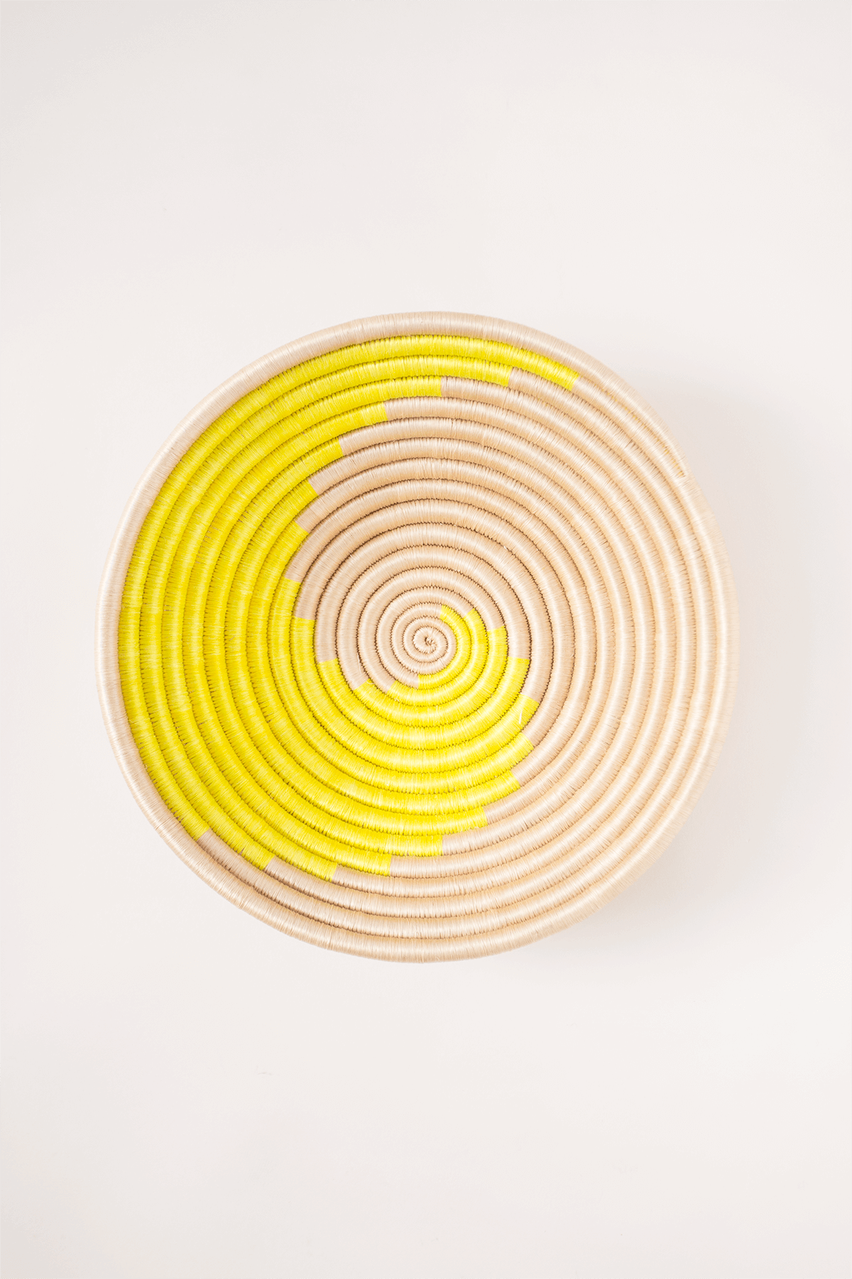 Woven basket with yellow and beige spiral pattern on a white background