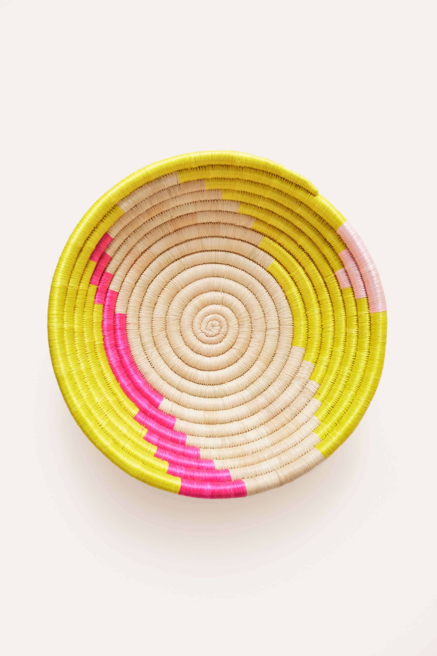 Woven basket with pink and yellow spiral pattern on a white background